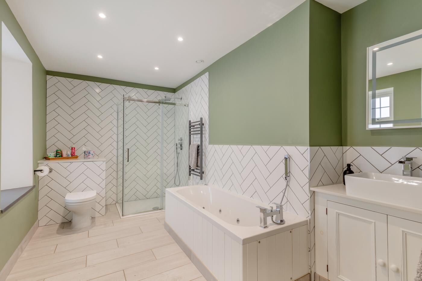 Un baño moderno con ducha, inodoro y bañera, que presenta un patrón de ziguezague en el suelo y paredes verdes.