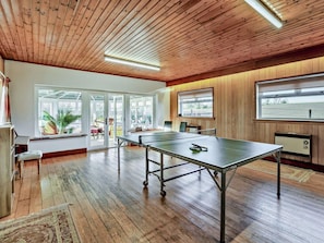 Una habitación con mesa de ping pong, suelo de madera, ventanas grandes y techo con vigas de madera.