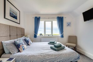 A bedroom with a bed, a window with curtains, a chair, and a flat-screen TV. - 1 Bed in Filey (oc-77710) (Hunmanby)