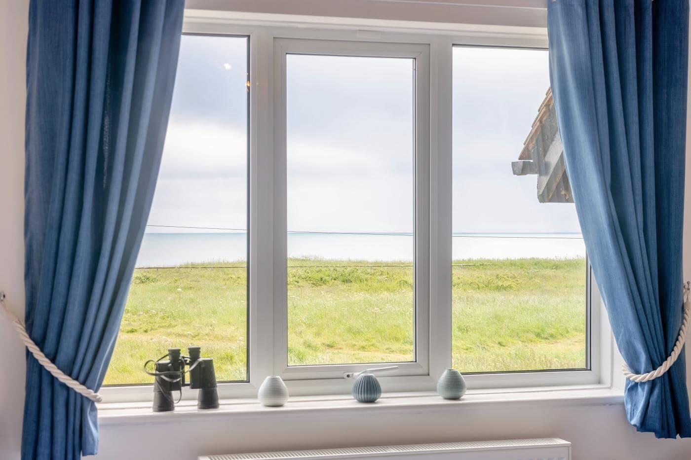 A room with a large window, curtains, binoculars, and a radiator.