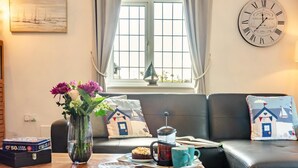 Uma sala de estar acolhedora com um sofá, uma mesa de centro com um bolo, um vaso de flores e um relógio de parede.
