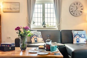 A cozy living room with a sofa, a coffee table with a cake, a vase of flowers, and a wall clock. - 1 Bed in Filey (oc-77710) (Hunmanby)
