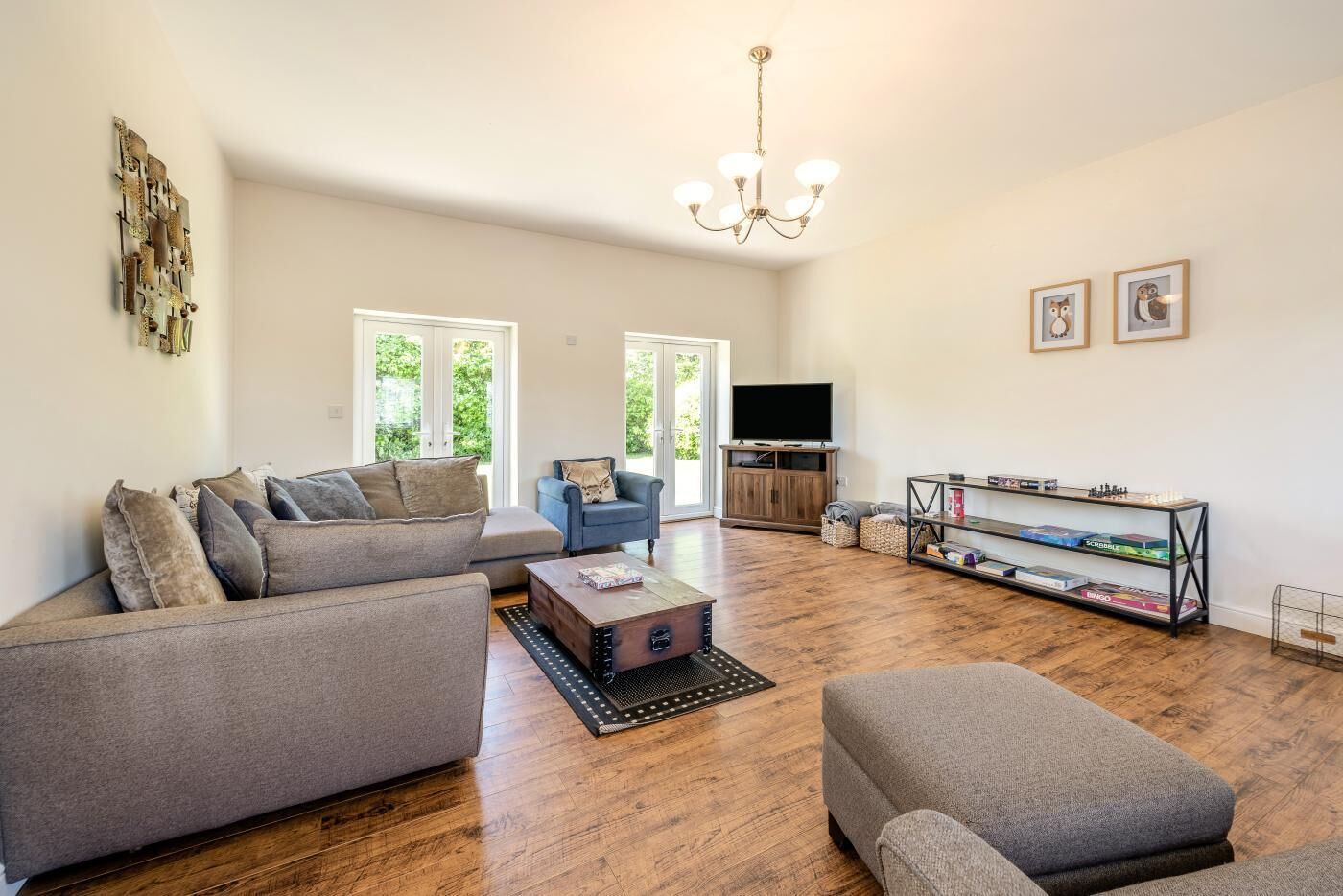 A spacious living room with a grey sofa, a blue armchair, a wooden coffee table, and a bookshelf.