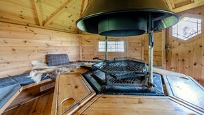 Ein Holzblockhaus-Interieur mit Kaminofen, einem mit Fell bezogenen Sitz und einem Fenster.