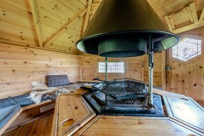 Ein Holzblockhaus-Interieur mit Kaminofen, einem mit Fell bezogenen Sitz und einem Fenster.