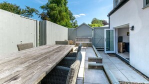 Un patio con una mesa de madera, sillas de mimbre, un cobertizo y la puerta de un garaje.