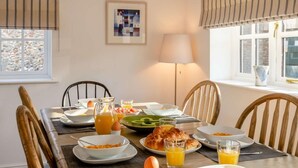 Un comedor con una mesa lista para el desayuno, con croissants, huevos y zumo de naranja.