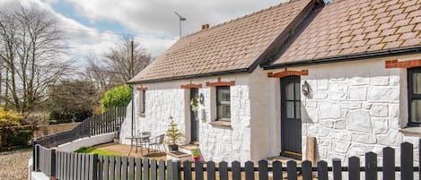 A stone house with a tiled roof, a fenced garden, and a clear sky.