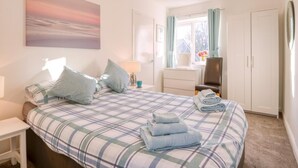 A bedroom with a bed, a nightstand, a lamp, a chair, a wardrobe, and a window with curtains. - 1 Bed in Filey (oc-77709) (Hunmanby)