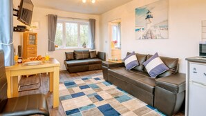 A cozy room with a sofa, a small table with breakfast items, a television, and a painting of a lighthouse. - 1 Bed in Filey (oc-77709) (Hunmanby)