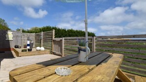 A wooden deck with a table and a blue umbrella, surrounded by a wooden fence and greenery. - 1 Bed in Filey (oc-77709) (Hunmanby)
