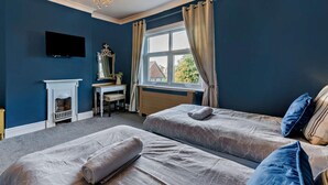 Ein Schlafzimmer mit zwei Betten, einem Schreibtisch, einem Spiegel, einem Kamin und einem Fernseher an der Wand.