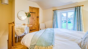 A bedroom with a bed, a wooden door, a mirror, a small table with a vase of flowers, and a window with curtains. - 3 Bed in Buxton (oc-77739) (Hartington)