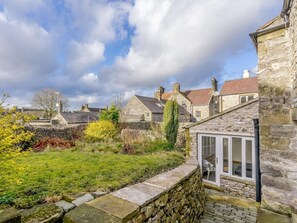 A stone building with a glass door entrance, surrounded by a stone wall and a grassy area. - 3 Bed in Buxton (oc-77739) (Hartington)