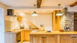 A kitchen with wooden cabinets, a stone wall, and pendant lighting. - 3 Bed in Buxton (oc-77739) (Hartington)