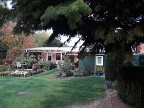 Ein Haus mit Backsteinfassade, einer Veranda und einem kleinen Garten mit verschiedenen Pflanzen und Rasenfläche.
