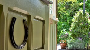 Una puerta verde con un picaporte negro, una ventana que ofrece vistas a un jardín con flores y un árbol.