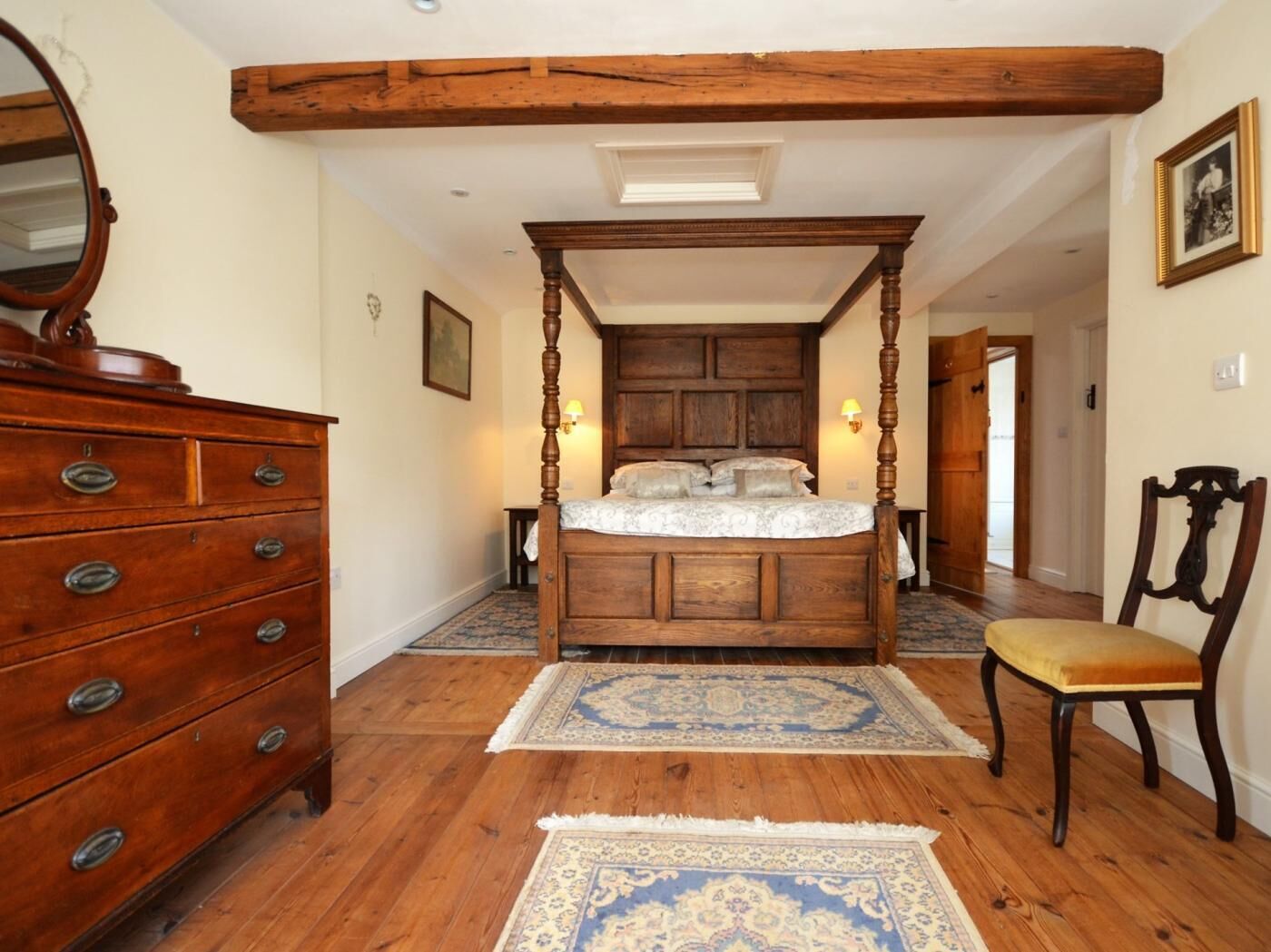 A bedroom with a four-poster bed, wooden dresser, and a chair.