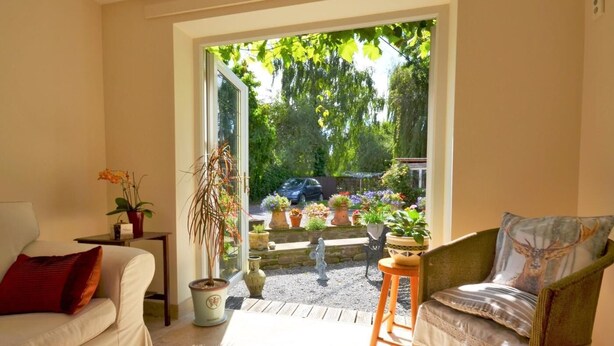 Una habitación acogedora con un sofá, una silla, una mesita y un ventanal a un jardín.