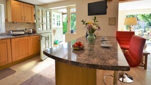Una cocina con armarios de madera, encimera de granito, frutero, un jarrón con flores y un televisor montado en la pared.