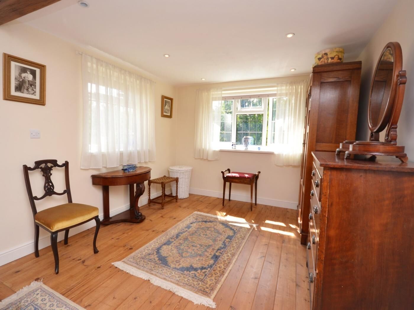 A room with wooden flooring, a wooden chair, a small table, a rug, a cabinet with a mirror, and a window with curtains.