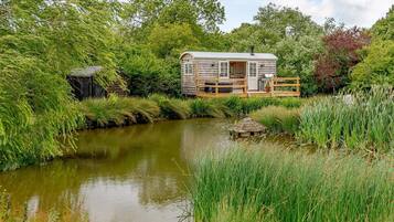 A cabin with a deck, a small shed, and a pond.