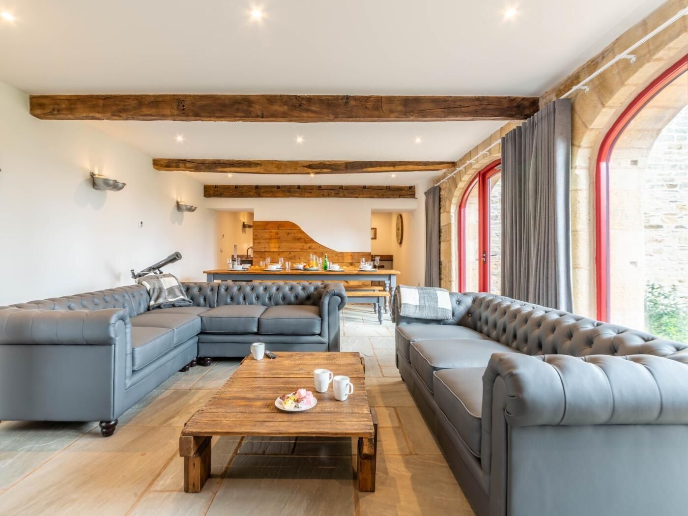 A spacious living area with a sofa set, a wooden coffee table, and a kitchen in the background.