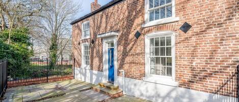 A brick house with a blue door, a small front garden, and a paved driveway.