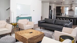 Un salon moderne avec un canapé, des fauteuils, une table basse et une cuisine en arrière-plan.