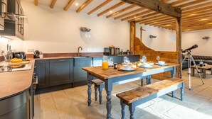 Une cuisine moderne avec un plafond en bois, une table à manger dressée pour quatre personnes et un télescope dans un coin.