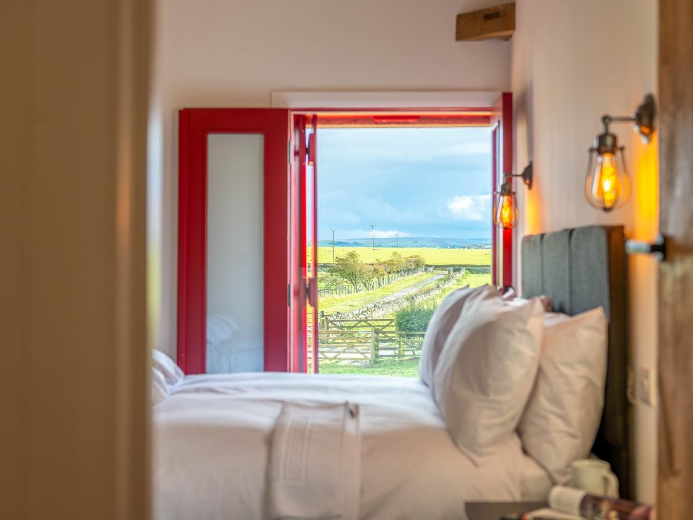 A bedroom with a bed, a view of a rural landscape, and a red door.