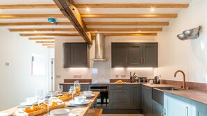 Une cuisine moderne avec des poutres en bois, des meubles de couleur sombre, une longue table en bois dressée pour le repas et un évier en acier inoxydable.