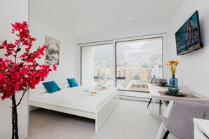A modern bedroom with a bed, a dining area, and a large window with a city view. - {Suite 406} Gym, Business Room, Modern, Relax (Lugano)