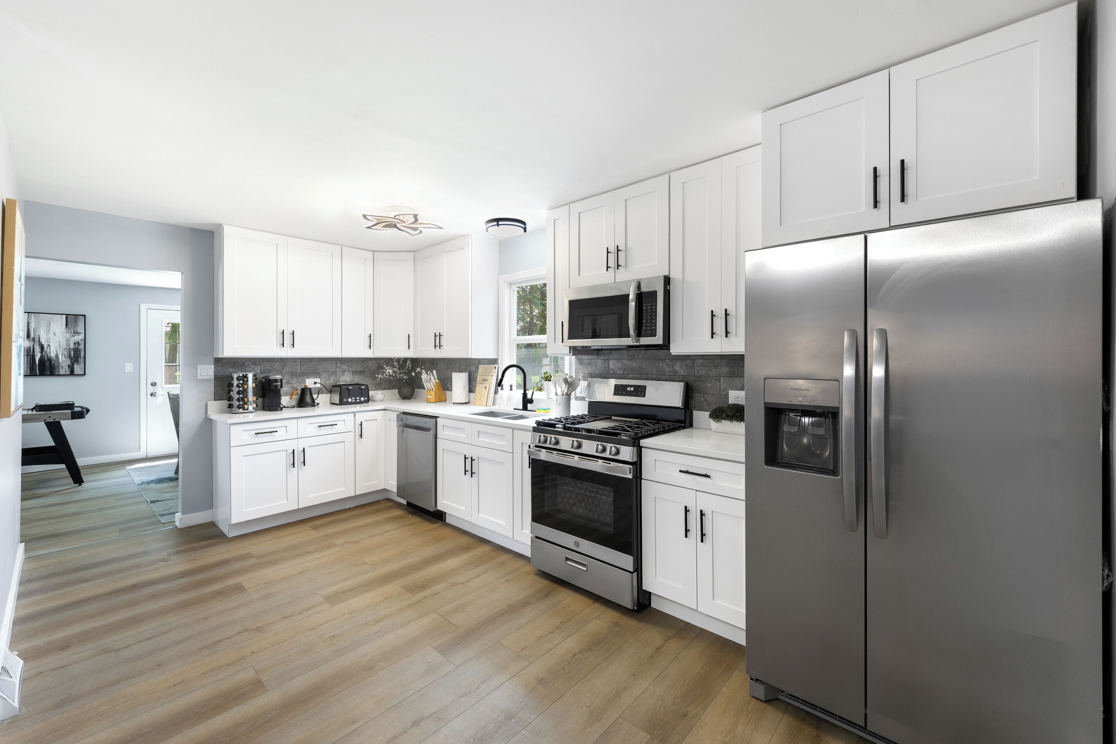 A modern kitchen with white cabinets, stainless steel appliances, and a wooden floor.