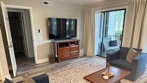 A living room with a flat-screen TV, a wooden cabinet, a sofa, a coffee table, and a patterned rug. - Fairway Vista - Newly Renovated with Beautiful Golf Course views, 1bed-1 bath (Pawleys Island)