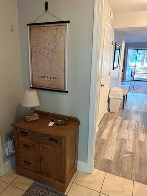 A hallway with a map of Pawleys Island, a wooden bench with a lamp, and a tiled floor. - Fairway Vista - Newly Renovated with Beautiful Golf Course views, 1bed-1 bath (Pawleys Island)