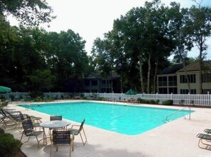 A swimming pool with lounge chairs and tables, surrounded by trees and a white fence. - Fairway Vista - Newly Renovated with Beautiful Golf Course views, 1bed-1 bath (Pawleys Island)