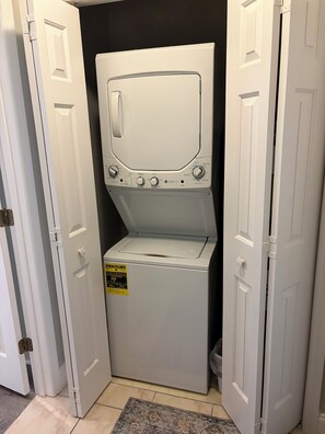 Máquina de lavar e secar de carregamento frontal com etiqueta ENERGY GUIDE, localizada em um corredor com portas brancas.