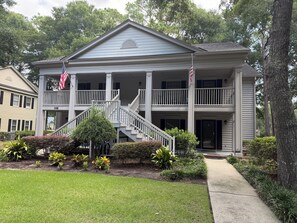 A two-story building with a central staircase, a covered porch, and a flag. - Fairway Vista - Newly Renovated with Beautiful Golf Course views, 1bed-1 bath (Pawleys Island)