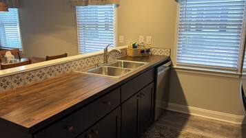 A kitchen with a wooden countertop, stainless steel sink, and dark cabinets.