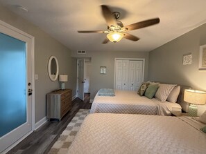 Een slaapkamer met twee bedden, een plafondventilator, een dressoir en een deur.