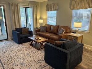 Een woonkamer met een bruine leren bank, twee fauteuils, een bijzettafeltje en een vloerkleed met een patroon.
