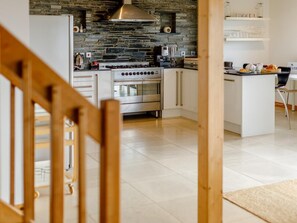 A modern kitchen with a stone backsplash, stainless steel appliances, and a wooden staircase. - 3 Bed in Crackington Haven (oc-78271) (Crackington)