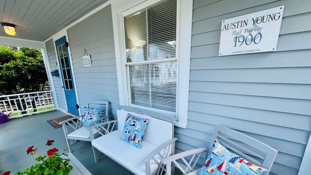 A porch with white furniture, a potted plant, and a sign indicating a historic site.
