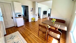 A kitchen with wooden flooring, a dining table with chairs, a yellow stool, and a microwave.