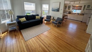 A living room with a sofa, two armchairs, a coffee table, and a kitchen area with cabinets and a refrigerator.