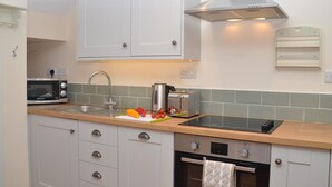 Una cocina con armarios blancos, una campana extractora de acero inoxidable, un microondas, un tostador y un fregadero con tabla de cortar y verduras.