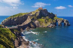 Une falaise côtière surmontée d’un bâtiment, une mer bleue et limpide, et un terrain rocheux.