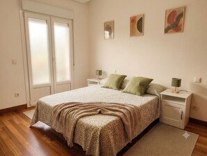 Une chambre à coucher comprenant un lit, deux tables de chevet, une commode, une porte et un mur orné de trois tableaux.