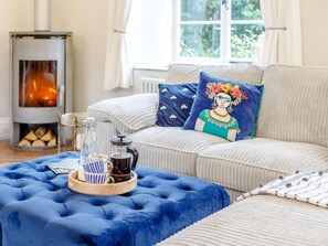 Ein gemütliches Wohnzimmer mit einer Couch, einem blauen Hocker, einem Couchtisch mit Tablett und einem Kamin.